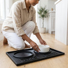 Person setting up a pet feeding station on a large black mat with 'FOOD' text.