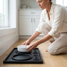 Woman placing a white bowl on a black tray in a kitchen.