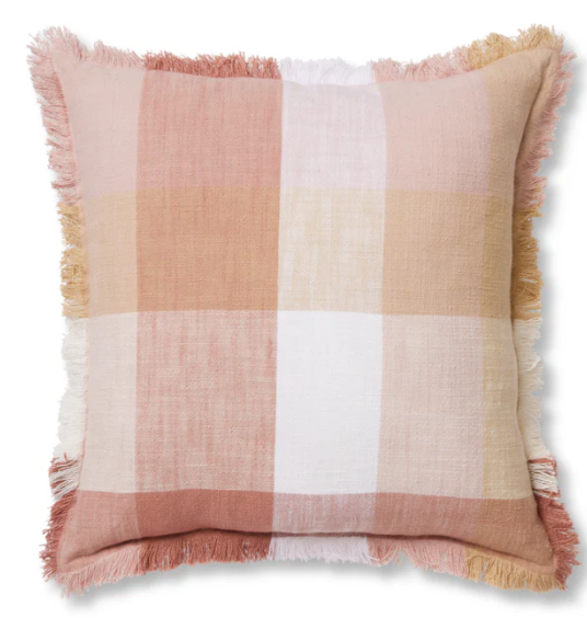 A square throw pillow with a soft plaid pattern in dusty pink, beige, white, and muted orange, finished with fringed edges.
