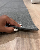Person's hand holding a gray rug edge on a wooden floor