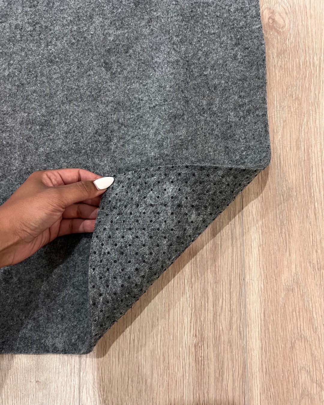 Gray carpet sample held by a hand on a wooden floor