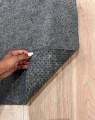Gray carpet sample held by a hand on a wooden floor