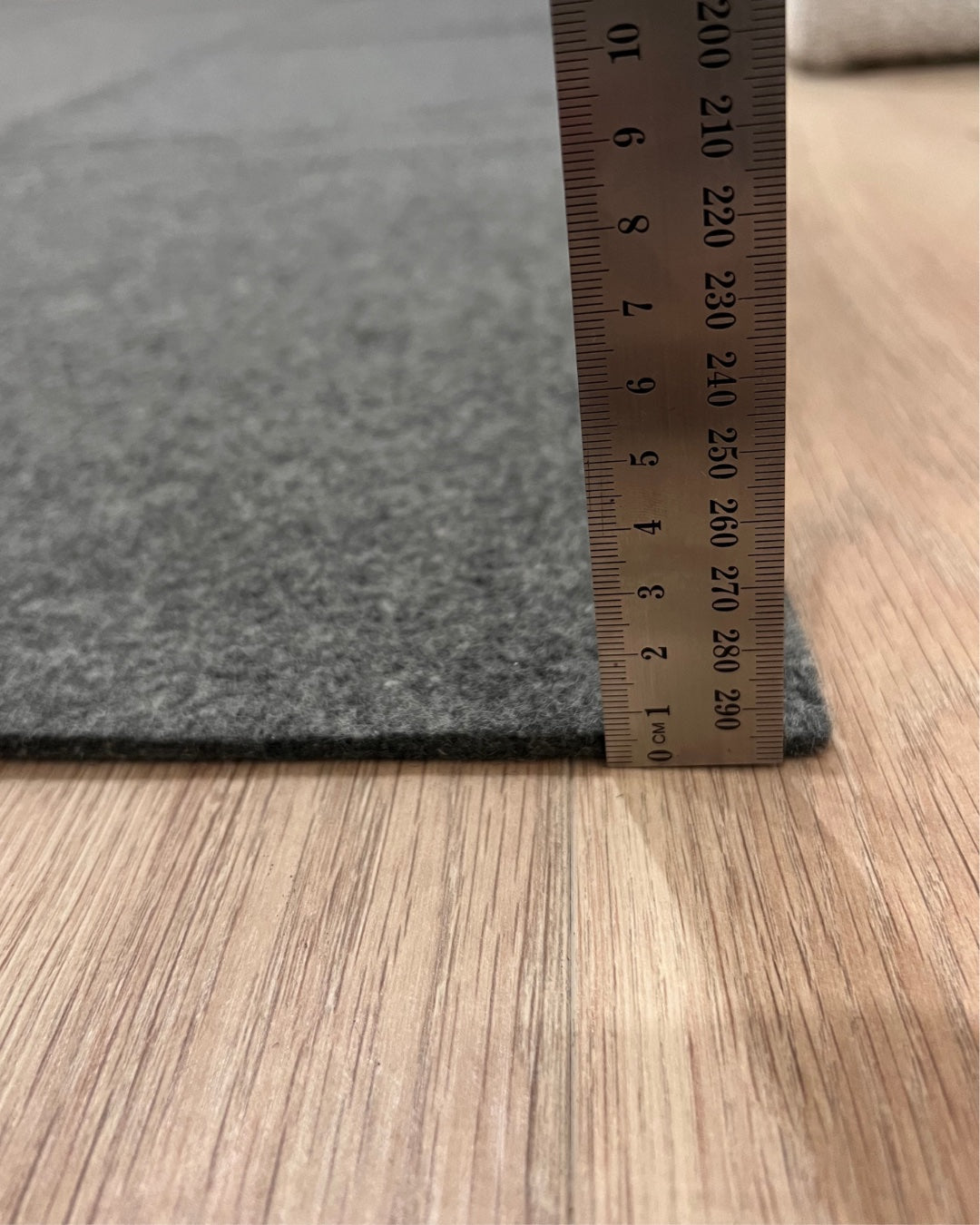 Gray carpet sample with a ruler for size reference on a wooden floor.