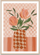 A framed art print featuring a stylized illustration of two peach-orange tulips with green leaves in a checkered terracotta and cream vase, set against a pink and peach checkered background.