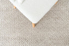 Close-up of a textured beige carpet with a white ottoman corner.