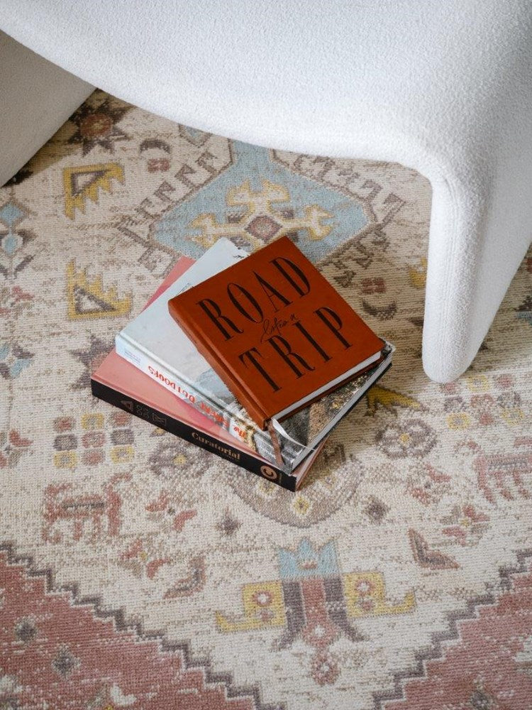 Stack of books on a patterned rug with a white chair partially visible