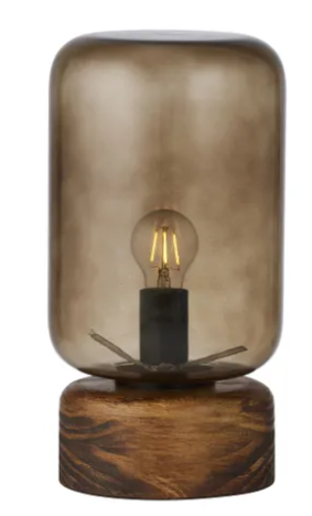 A table lamp with a smoky translucent glass shade and a round dark wood base, shown against a plain white background.
