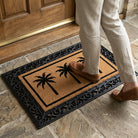 Person stepping onto a doormat with palm tree design at the entrance of a building.
