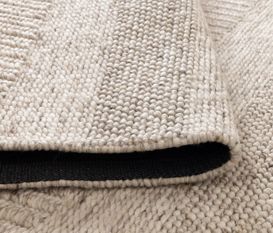 Close-up of a beige textured rug with a black border.