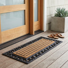 Doormat on a wooden floor outside a house with sandals and a plant nearby.