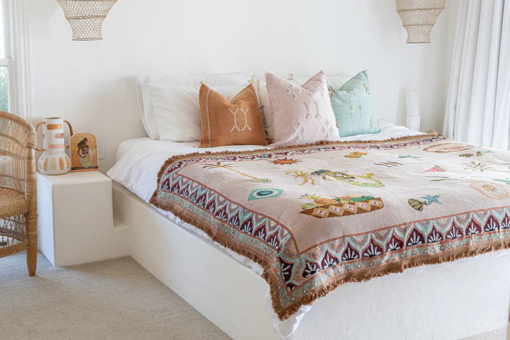 Bedroom with a bed featuring a patterned throw and pillows, next to a wicker chair.