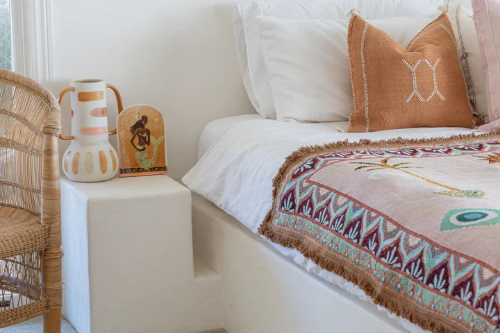 Bedroom with a bed featuring patterned throw and pillows, a nightstand with decorative items, and a chair.