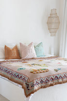 Bed with patterned quilt, colorful pillows, and a hanging lamp in a bedroom setting.