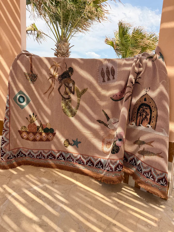 Decorative throw blanket with mermaid and fish designs draped over a chair outdoors.