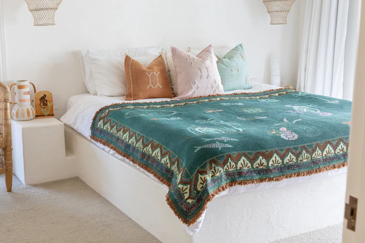 Bed with a green patterned throw and colorful pillows in a bedroom setting.