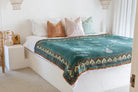 Bed with a green patterned throw and colorful pillows in a bedroom setting.
