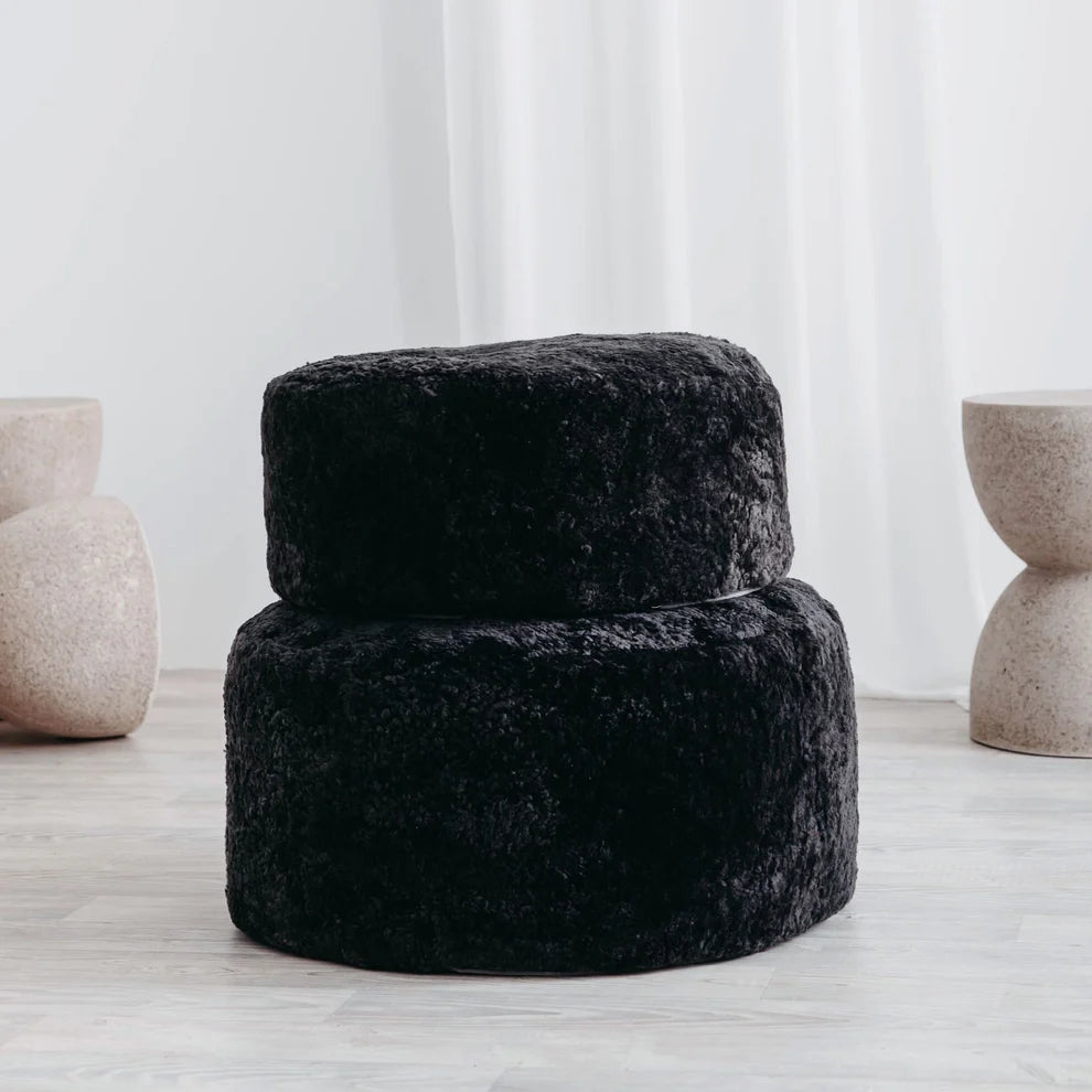 Black textured ottoman in a minimalistic room with light-colored floor and white walls.