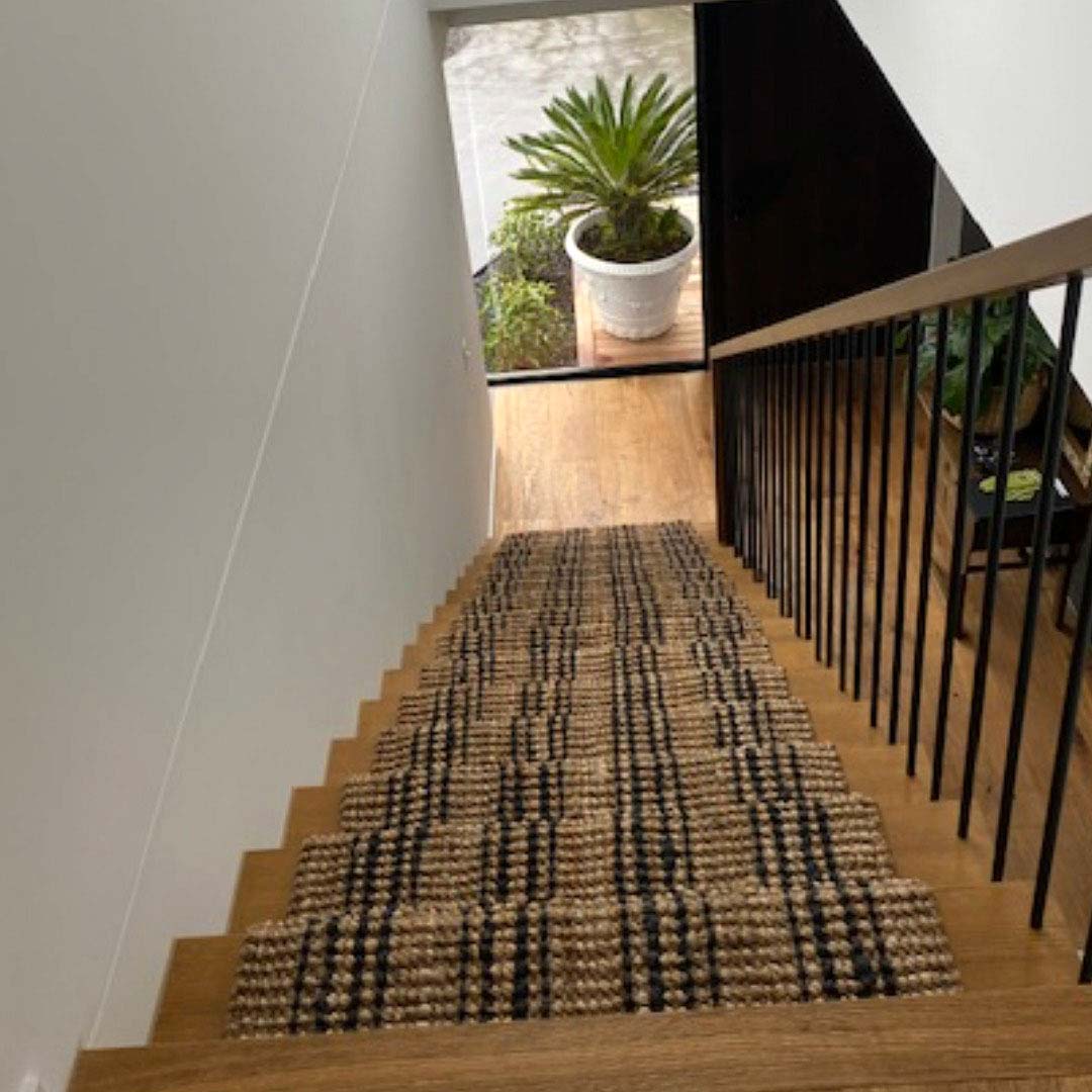 Staircase with a textured runner leading to an outdoor area with plants.