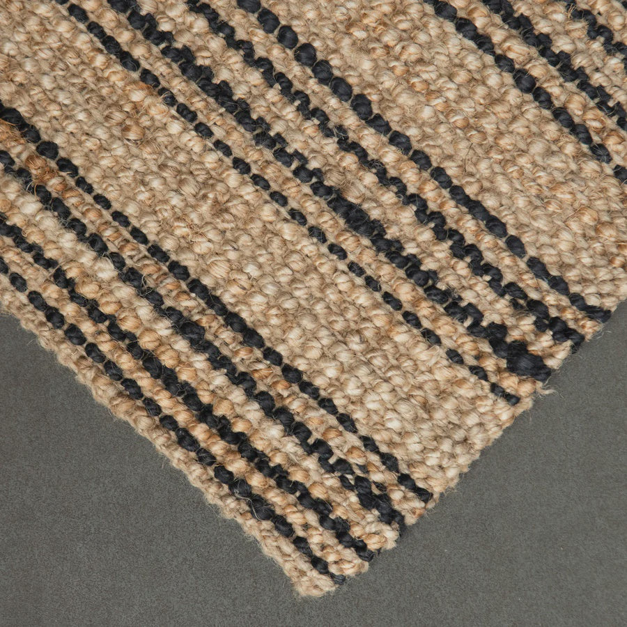Close-up of a woven jute rug with black lines on a gray background