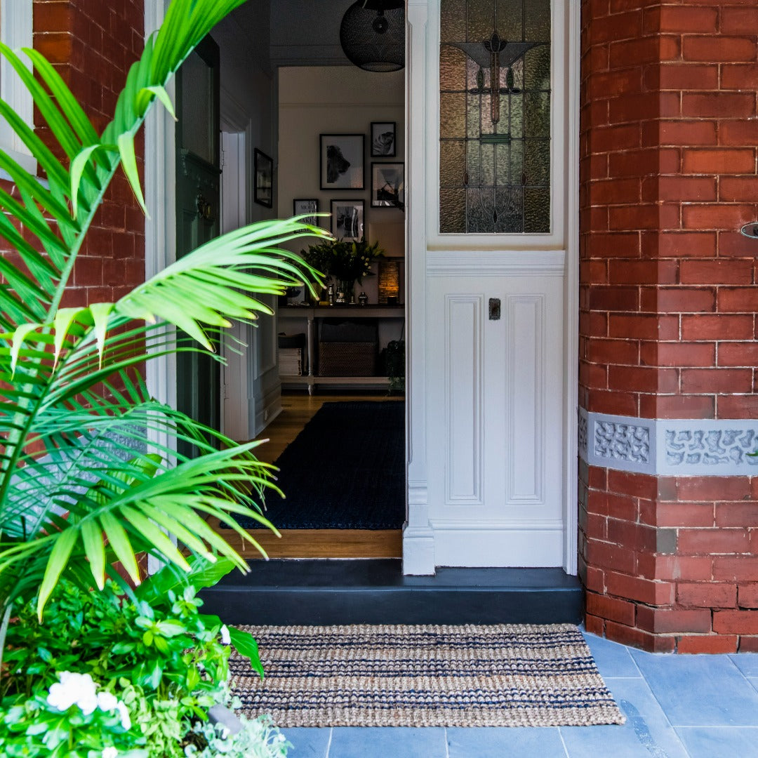 Front door of a house with a doormat, plants, and a view into the interior.