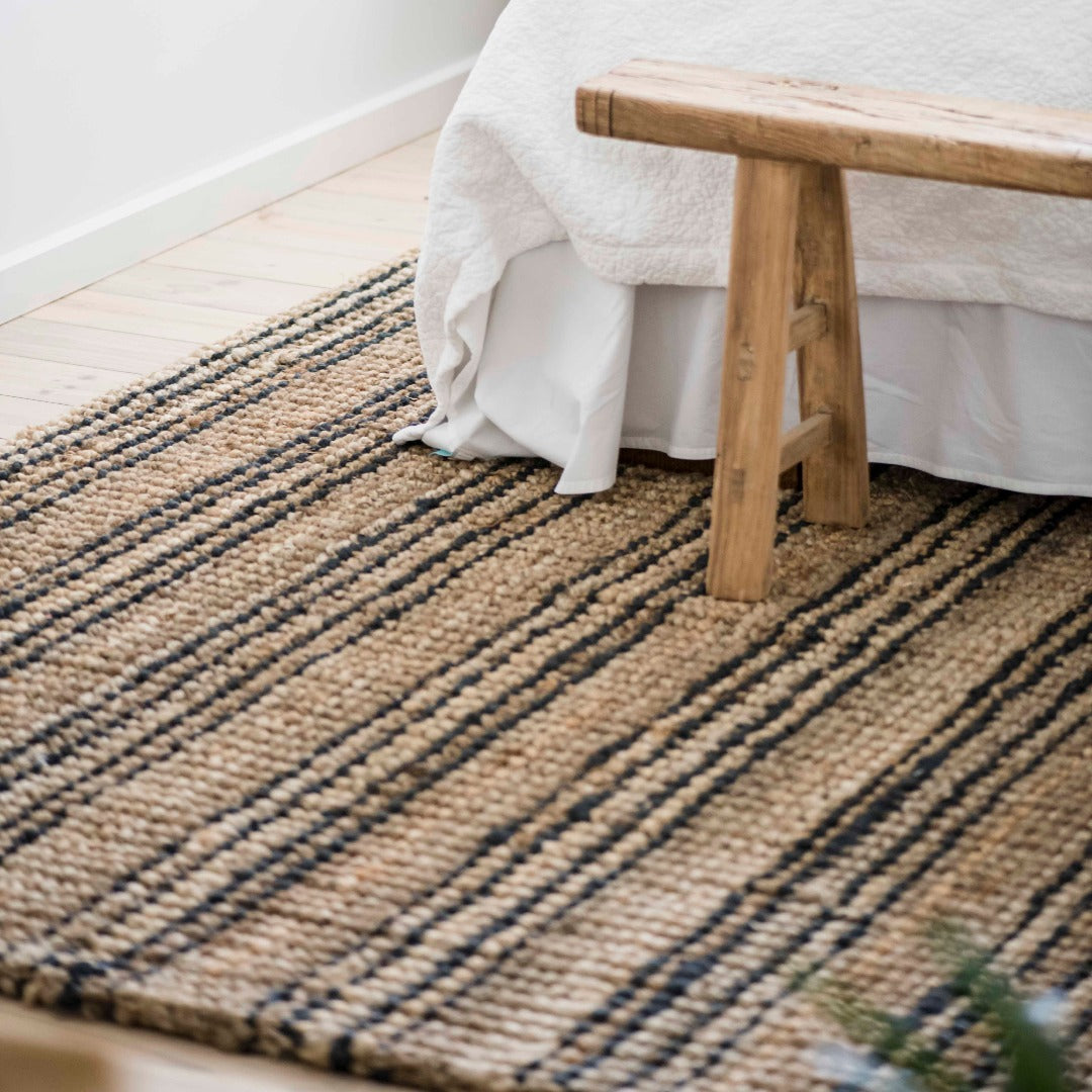 Woven jute rug with a wooden bench and white fabric in a room setting.