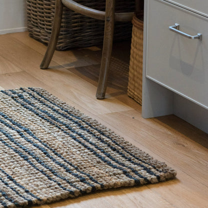Textured rug with blue and beige stripes on a wooden floor next to a wicker basket and white cabinet.