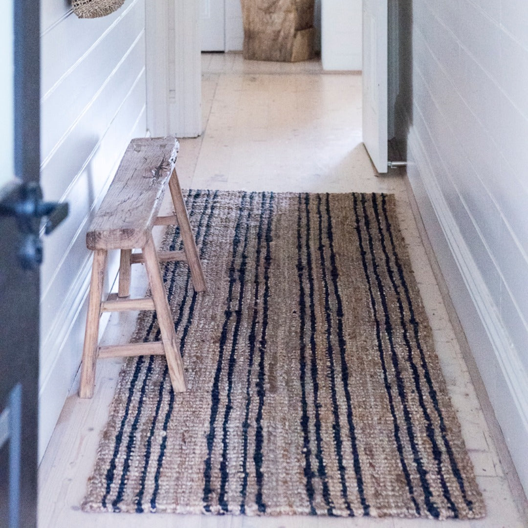 Striped rug on a wooden floor with a wooden stool in a room.