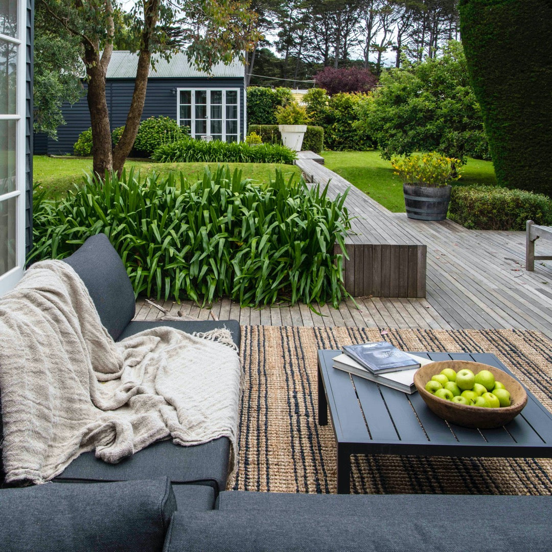 Outdoor patio with gray sofa, coffee table, and green apples on a wooden deck.