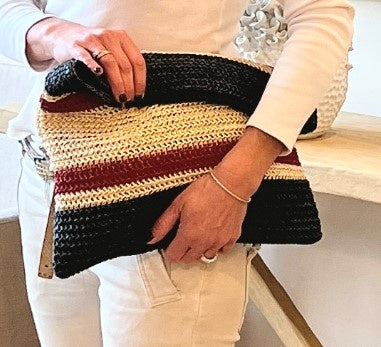 Person holding a striped woven clutch bag with black, red, and beige colors.