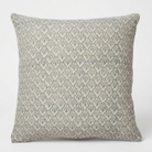 A square throw pillow featuring a repeating block-printed damask pattern in muted sage green and light gray on a warm off-white background.