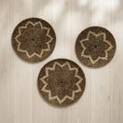 Three round woven wall baskets with starburst patterns in natural brown and beige, arranged on a light wood plank wall.