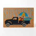 A rectangular coir doormat featuring a black pickup truck carrying a blue and yellow beach umbrella and a striped surfboard, with the word 'SUNSHINE' in large gray letters across the top.