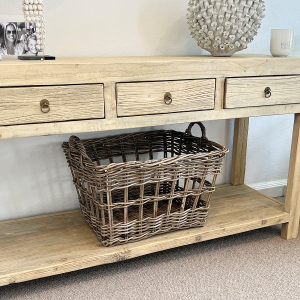 Light wooden console table with a wicker basket on a carpeted floor.