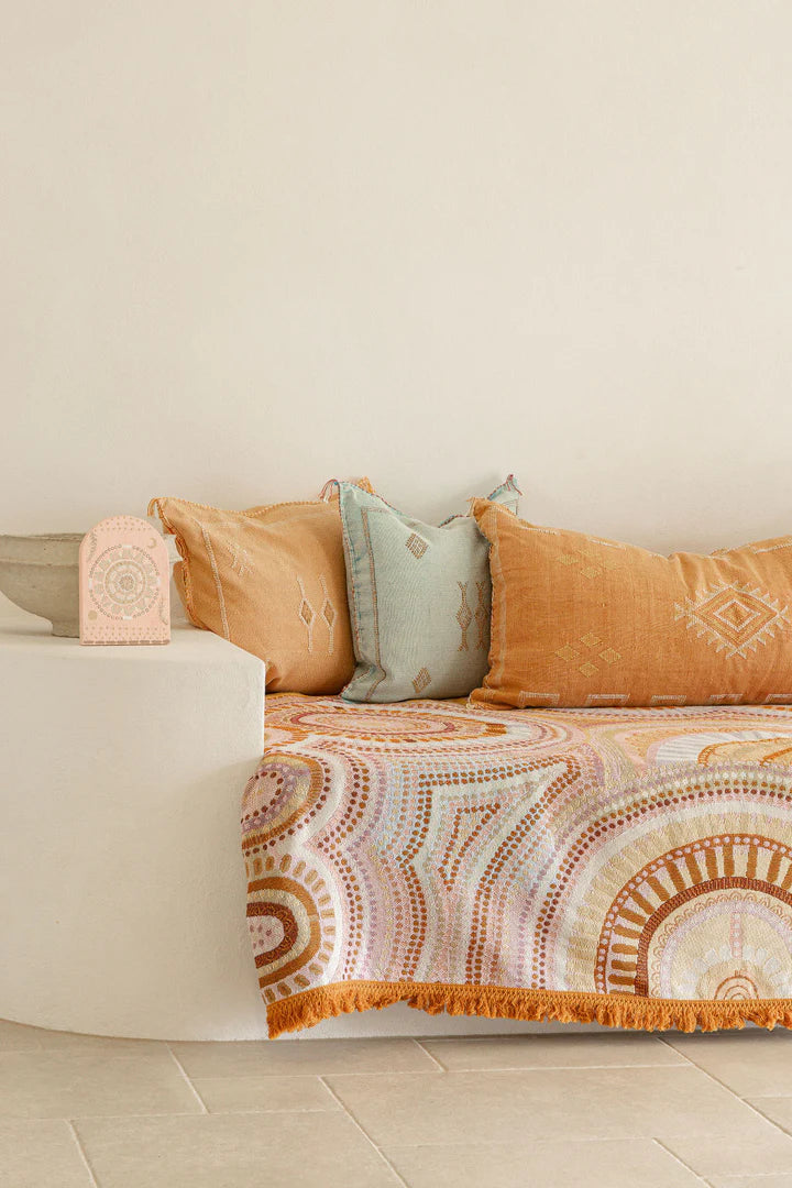 Decorative throw blanket with geometric pattern on a sofa against a beige wall.