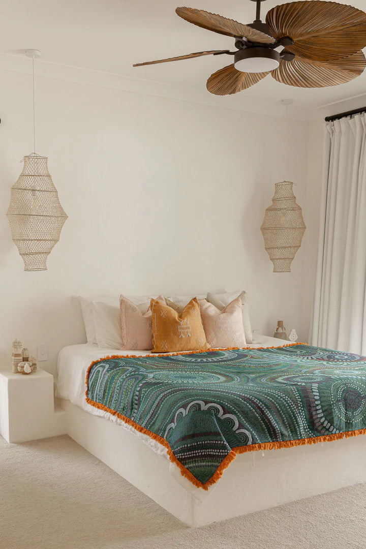Bedroom with a bed featuring a green and orange patterned blanket, surrounded by decorative lamps and a ceiling fan.