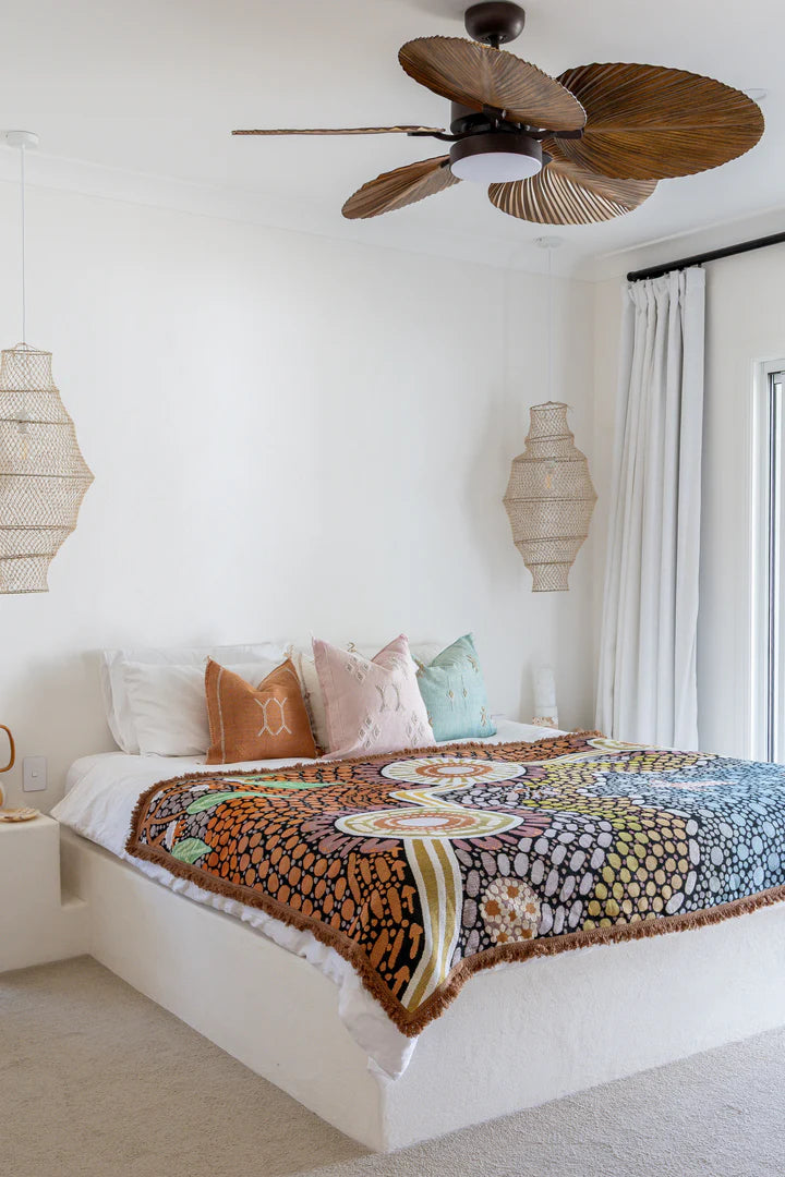 Bedroom with a colorful patterned blanket on a bed, wooden ceiling fan, and decorative lamps.