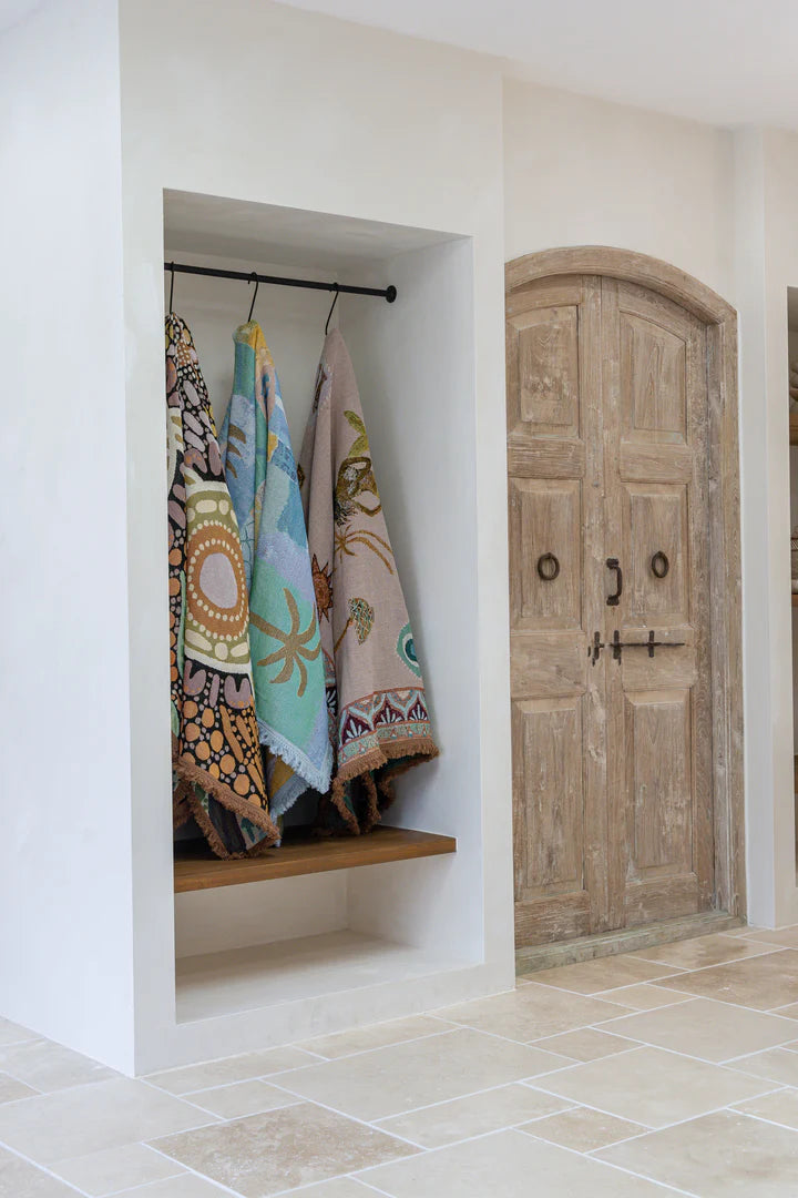 Closet with throw rugs hanging on a rack and a wooden door in the background.