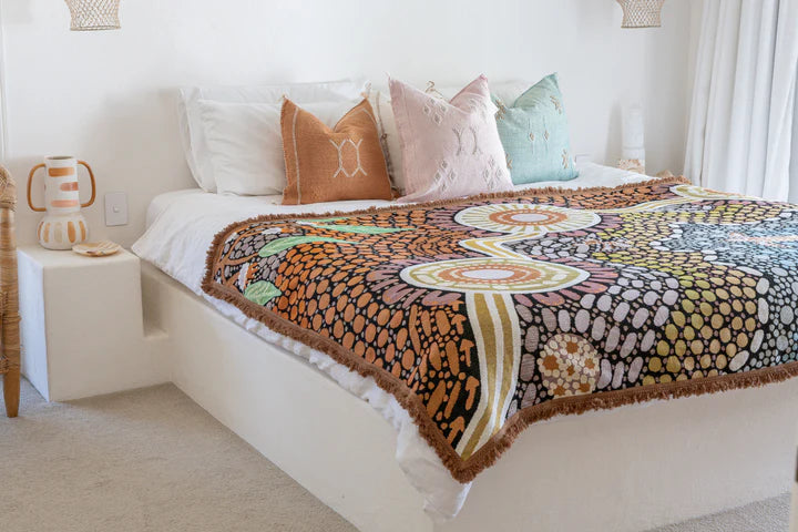 Bed with a colorful patterned throw blanket and decorative pillows in a bedroom setting.