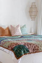 Colorful patterned blanket on a bed with decorative pillows against a white wall.
