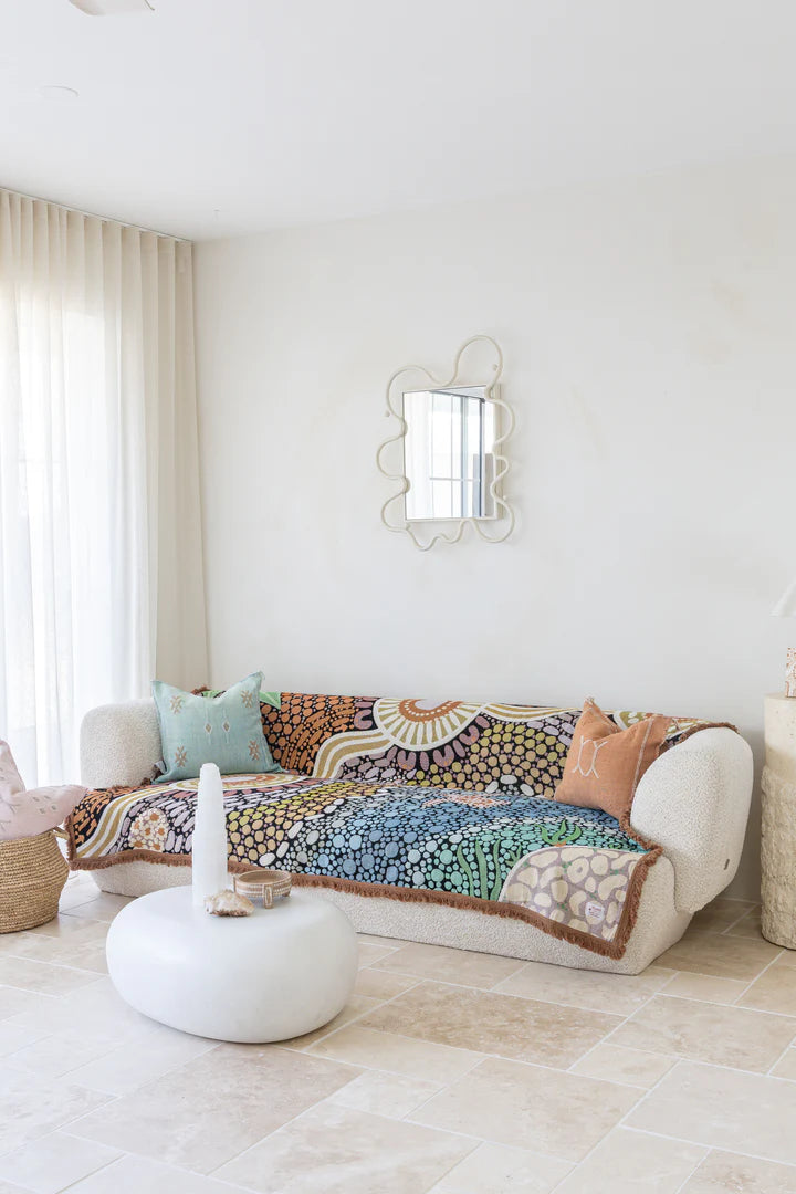 Decorative quilt on a white sofa in a bright living room with a mirror and cushions.