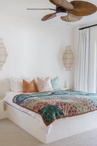 Bedroom with a bed featuring a colorful blanket and pillows, wooden ceiling fan, and decorative lamps.