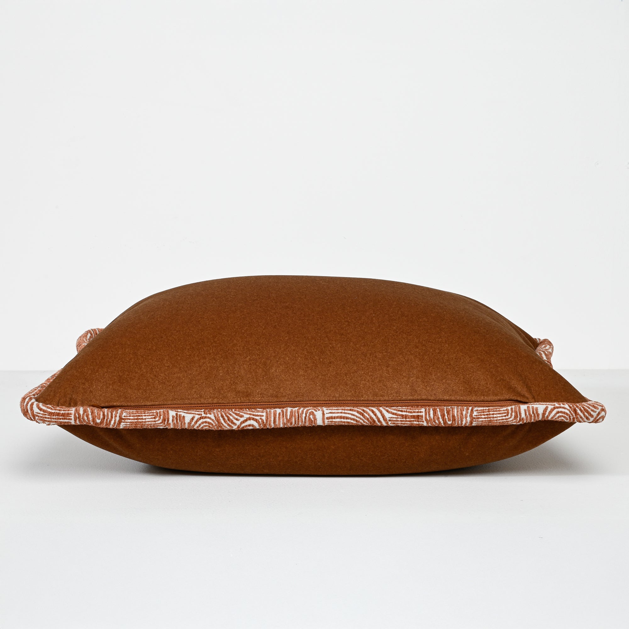 A square brown throw pillow with a patterned border trim, photographed against a clean white studio background.