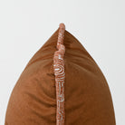 A close-up of a brown textured throw pillow with a decorative vertical tufted trim featuring a white and terracotta pattern, set against a plain light gray background.