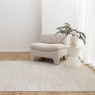 Beige armchair and side table with a plant in a minimalistic room.