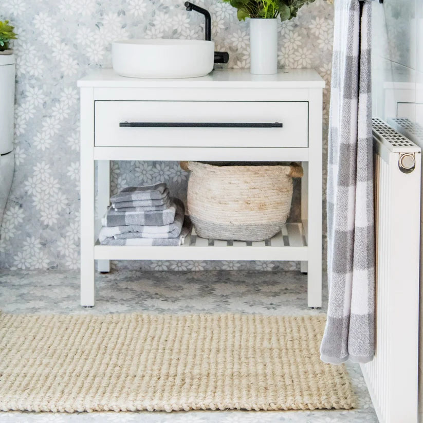 Bathroom with white vanity, towels, and a rug on a light gray floor.
