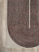 A close-up of a textured area rug featuring a modern U-shaped design with concentric arches in dark brown and beige on a light beige base.