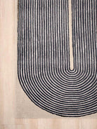 Close-up of a modern area rug with a U-shaped design featuring concentric arches in black on a beige background, shown on a light wood floor.