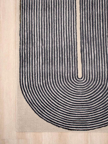 Close-up of a modern area rug with a U-shaped design featuring concentric arches in black on a beige background, shown on a light wood floor.