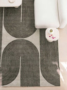 Gray area rug with black abstract patterns on a light-colored floor.