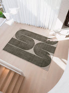 A rectangular area rug with a modern abstract design of two large winding dark gray loops on a light beige background, styled on a light wood staircase landing.